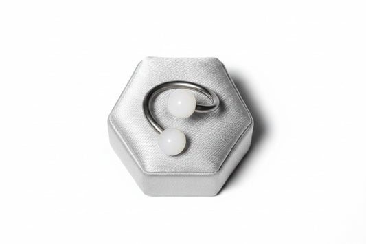 White Acrylic Glow Curled Barbell in 316l stainless steel on a silver silk jewelry display.
