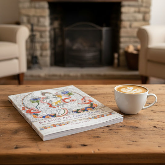 Oriental Sacred Buddha Mentally Relaxing Adult Coloring Book on a wooden table sitting next to a cup of coffee in a cozy living room setting.