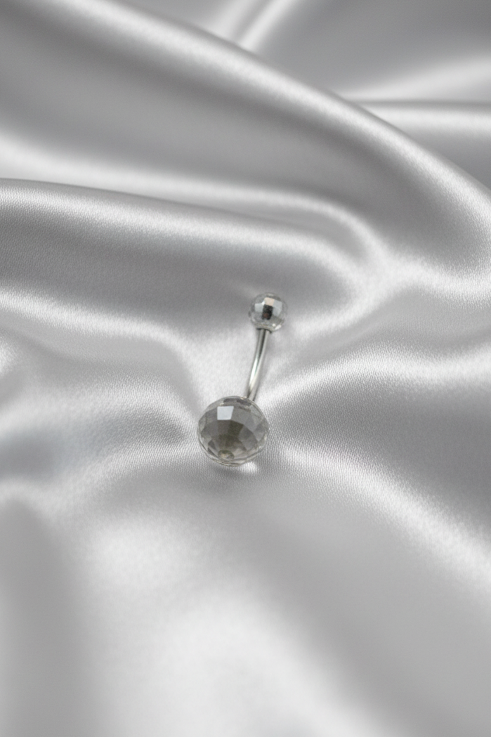 Clear Acrylic Disco Ball Belly Button Ring in 316l stainless steel on silver silk fabric.