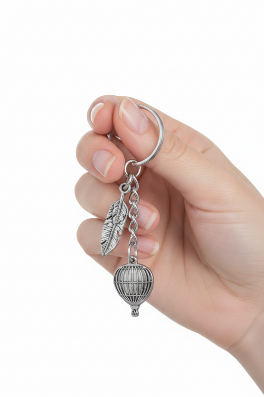 Hot Air Balloon and Feather Handmade Pewter Charm Keychain held in a hand showing scale.