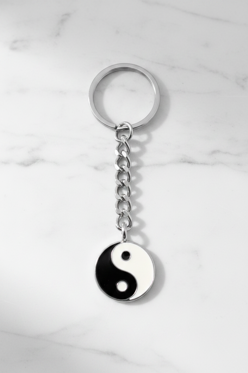 Black and White Enamel Yin Yang Handmade Pewter Charm Keychain on a white marble surface.