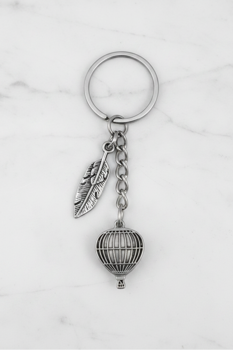 Hot Air Balloon and Feather Handmade Pewter Charm Keychain on a white marble surface.