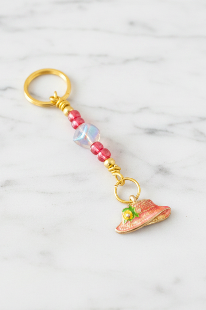 Red Enamel Hat Handmade Beaded Mini Keychain on a white marble surface.
