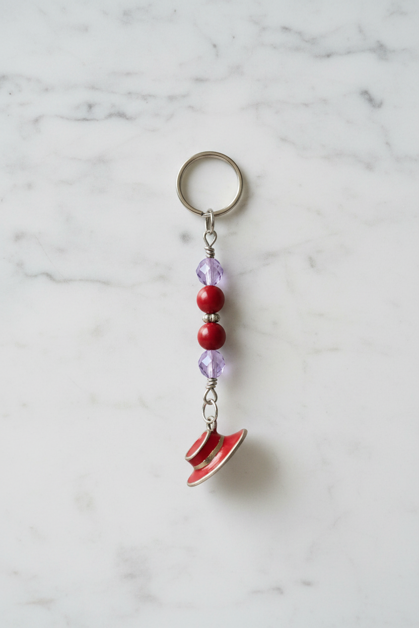 Red Enamel Hat Handmade Beaded Mini Keychain on a white marble surface.