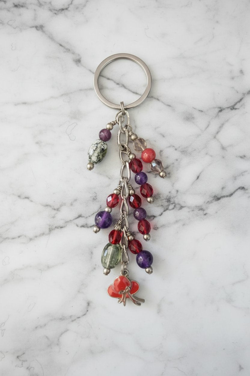 Little Red Enamel Hat Handmade Beaded Keychain on a white marble surface.