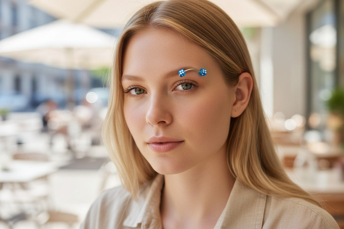 Cloud 9 Mystic Gifts blue acrylic dice eyebrow ring worn by a blonde woman in a casual outdoor setting